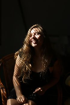 Portrait of young beautiful woman sitting in chair, striped shadows. Concept of female beauty and home photo session.