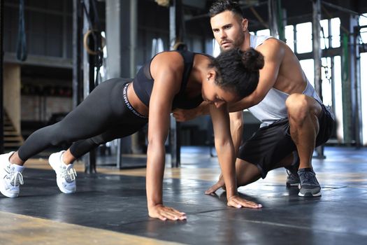 Sporty woman doing push-up in a gym, her boyfriend is watching her