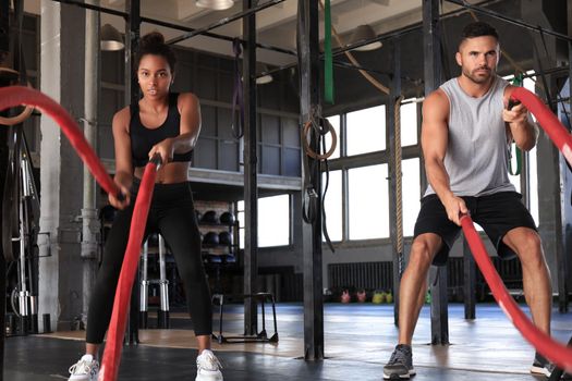 Athletic young couple with battle rope doing exercise in functional training fitness gym