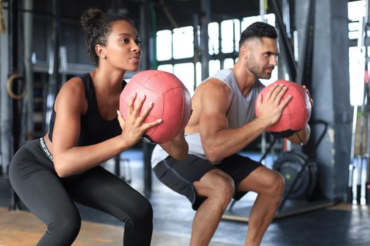 Beautiful young sports couple is working out with medicine ball in gym