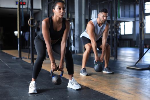 Fit and muscular couple focused on lifting a dumbbell during an exercise class in a gym