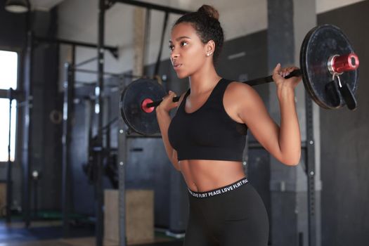 Beautiful woman exercising squatting with barbell at gym