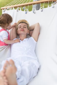 Happy mother and a little daughter enjoying free time hugging and relaxing in a hammock during a sunny day on holiday home garden