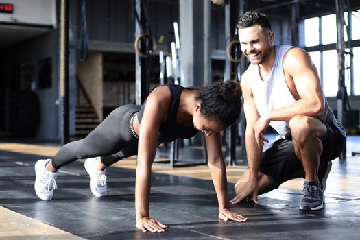 Sporty woman doing push-up in a gym, her boyfriend is watching her