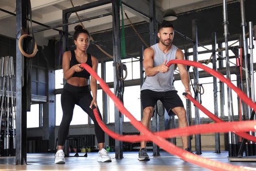 Athletic young couple with battle rope doing exercise in functional training fitness gym