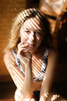 Portrait of young blonde woman wearing bra, striped shadows. Concept of beautiful female person and home photosession.