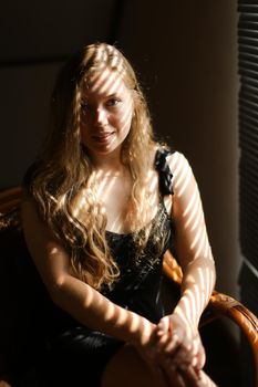 Portrait of young caucasian woman sitting in chair, striped shadows. Concept of female beauty and home photo session.