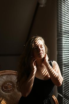 Portrait of young european woman sitting in chair, striped shadows. Concept of female beauty and home photo session.