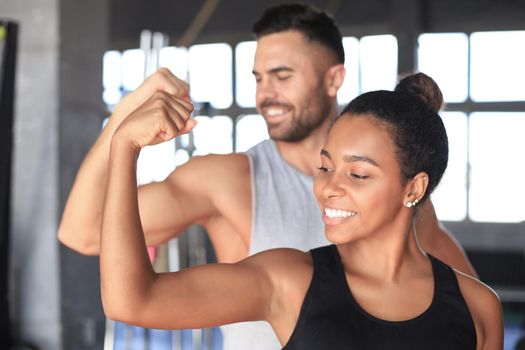 Cheerful sportive couple training together and showing biceps at the gym