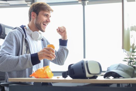 Portrait of ecstatic gamer guy in headphones screaming and rejoicing while playing video games on computer