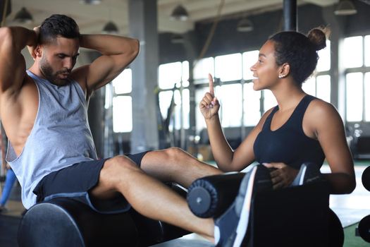 Trainer helping young man to do abdominal exercises in gym