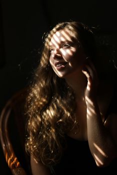 Portrait of american european woman sitting in chair, striped shadows. Concept of female beauty and home photo session.