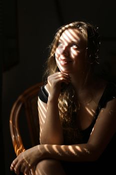 Portrait of young pretty woman sitting in chair, striped shadows. Concept of female beauty and home photo session.