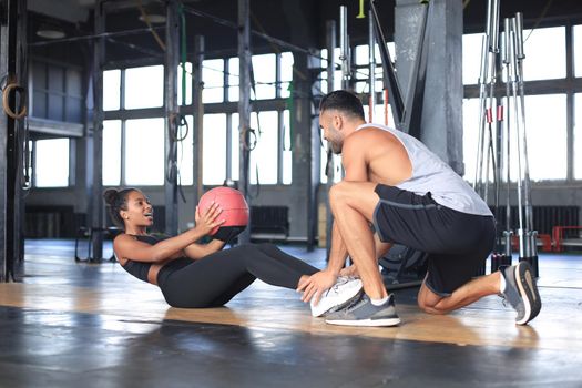 Trainer helping young woman to do abdominal exercises in gym