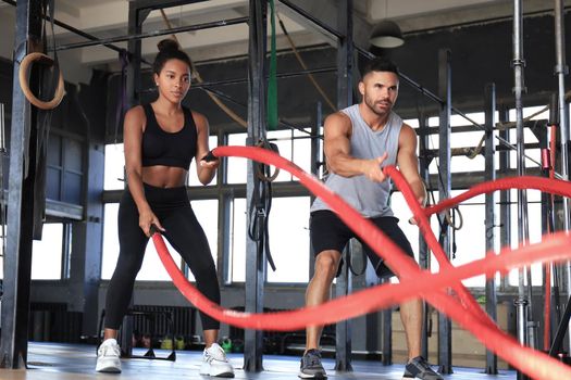 Athletic young couple with battle rope doing exercise in functional training fitness gym