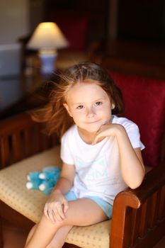 Little pretty female kid sitting with toy in wooden chair. Concept of kid model and wood in interior.