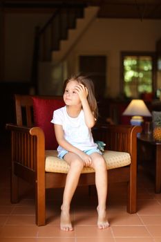 Female american kid sitting in wooden chair in living room. Concept of child model and cozy interior.