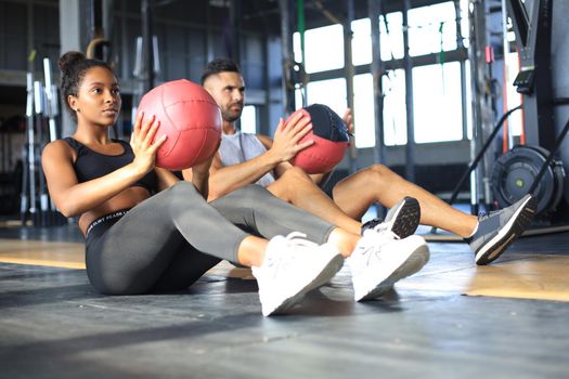 Beautiful young sports couple is working out with medicine ball in gym