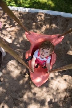 cheerful smiling cute little girl having fun while swinging  on a playground  in the park