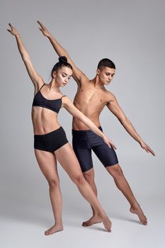 A pair of sexy ballet dancers in black suits are posing over a gray studio background. Attractive man in black shorts and beautiful woman in a black swimwear are dancing together. Ballet and contemporary choreography concept. Art photo.