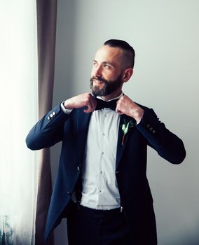 happy groom straightening his bow tie and looking out the window. people and events