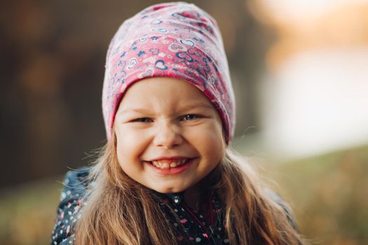 Portrait of happy pretty little girl in jacket and hat spending time in park. Childhood and happiness concept