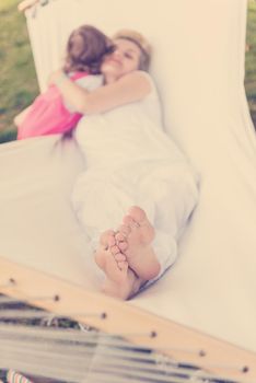 Happy mother and a little daughter enjoying free time hugging and relaxing in a hammock during a sunny day on holiday home garden