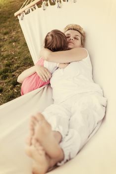 Happy mother and a little daughter enjoying free time hugging and relaxing in a hammock during a sunny day on holiday home garden