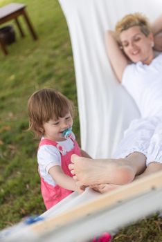 Happy mother and a little daughter enjoying free time hugging and relaxing in a hammock during a sunny day on holiday home garden