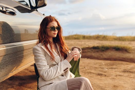 beautiful woman sitting on a chair in a field wearing dark glasses near the car endless field. High quality photo