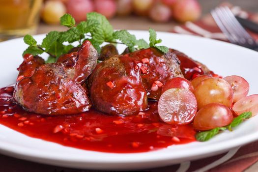 Warm salad with chicken liver and grapes on the plate. Warm salad from turkey liver. Warm salad with chicken liver in raspberry sauce.