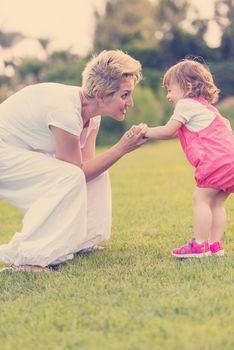 Young Mother and cute little daughter enjoying free time playing outside at backyard on the grass, happy family in nature concept