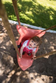 cheerful smiling cute little girl having fun while swinging  on a playground  in the park