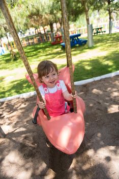 cheerful smiling cute little girl having fun while swinging  on a playground  in the park