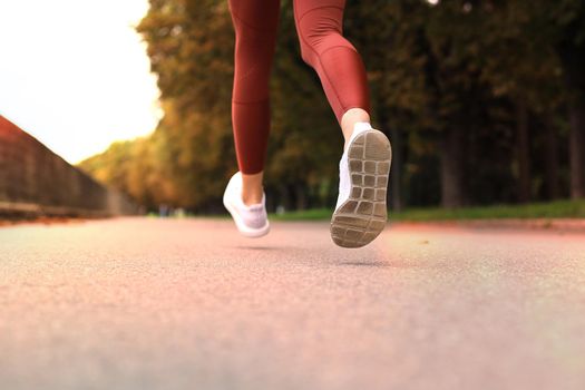 Runner feet running on road closeup on shoe, outdoor at sunset or sunrise