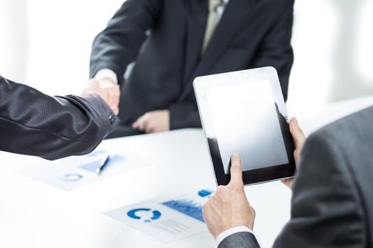 close up.businessman with a digital tablet on the background of a handshake of business partners