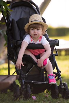 little and very beautiful baby girl sitting in the baby stroller and waiting for mom