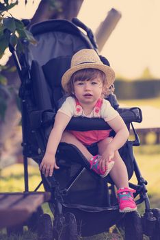 little and very beautiful baby girl sitting in the baby stroller and waiting for mom