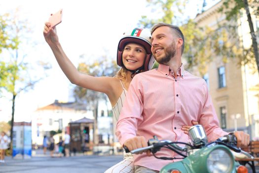 Happy young couple taking selfie on smartphone while sitting on scooter outdoors