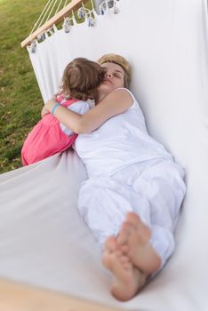 Happy mother and a little daughter enjoying free time hugging and relaxing in a hammock during a sunny day on holiday home garden