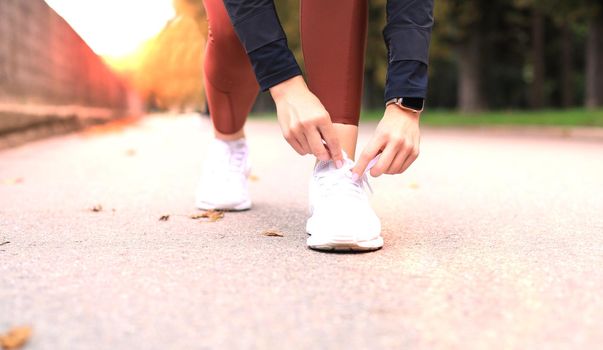 Closeup of unrecognizable sport woman tying sports shoes during evening run outdoors