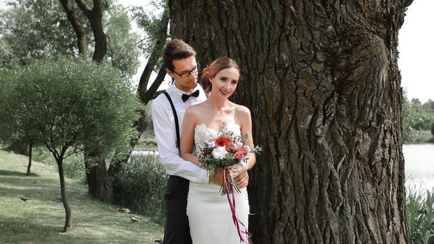 happy bride and groom standing near a big tree in the city Park.