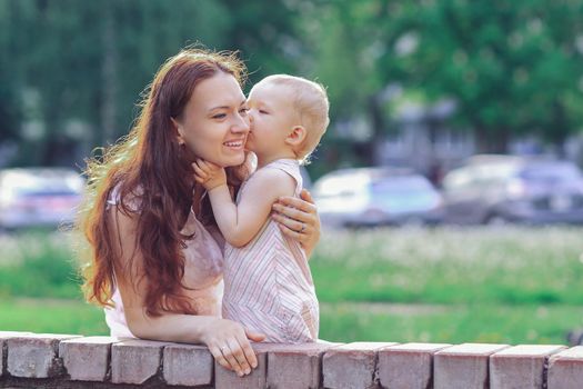 little girl kisses her mommy while walking in the Park.the concept of happy motherhood