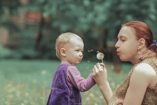 close up.a young mother teaches her little daughter to blow on a dandelion.