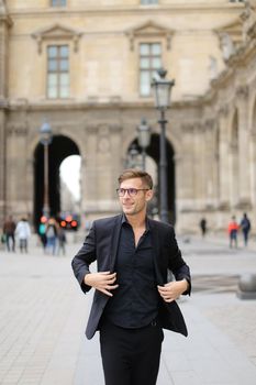 Young man in glasses walking in Paris and wearing black suit, France. Concept of walking in city and male fashion.