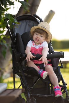 little and very beautiful baby girl sitting in the baby stroller and waiting for mom