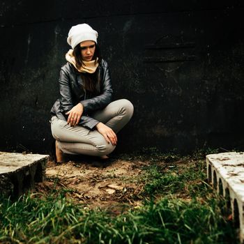 sad young woman sitting near black wall. sad depression