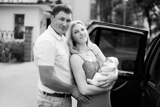 photo in retro style.portrait of happy young parents with newborn baby standing near the car