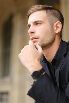 Closeup portrait of young man wearing black suit and watch. Concept of successful businessman and male model.