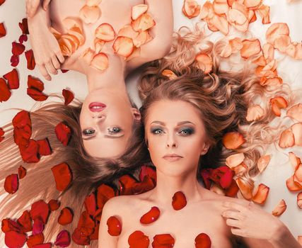 two beautiful young women relaxing lying among rose petals. the concept of a healthy lifestyle